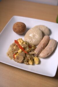 Traditional Jamaican ackee and saltfish with boiled dumplings, green bananas, and a fried dumpling on a white plate.