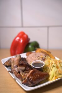 Jamaican jerk chicken served with rice and peas, fried plantains, steamed cabbage, and jerk sauce on the side.